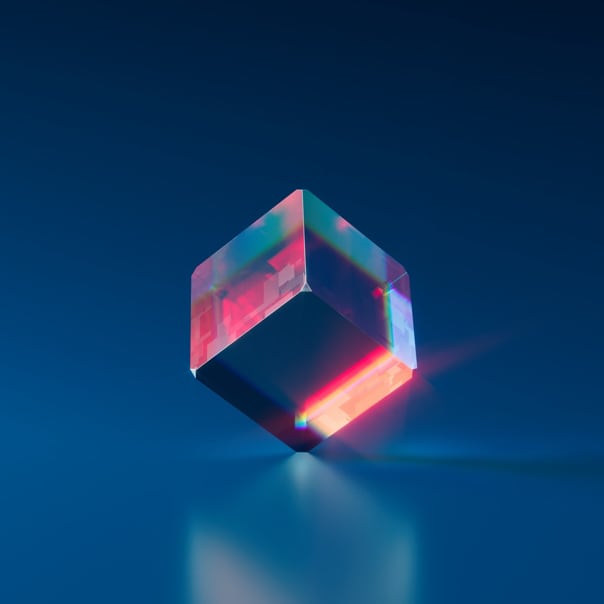 A Glass cube balanced on its point with red light reflected in it and a light blue to dark blue gradient background with a blurred reflection of it on the floor.